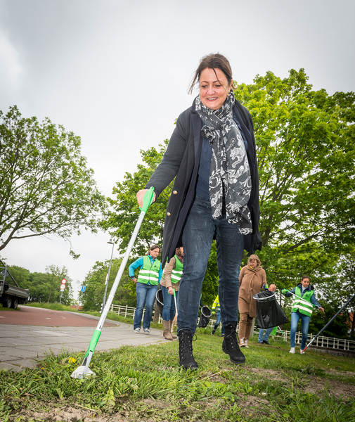 Een vrouw met een jas aan prikt afval met afvalgrijper